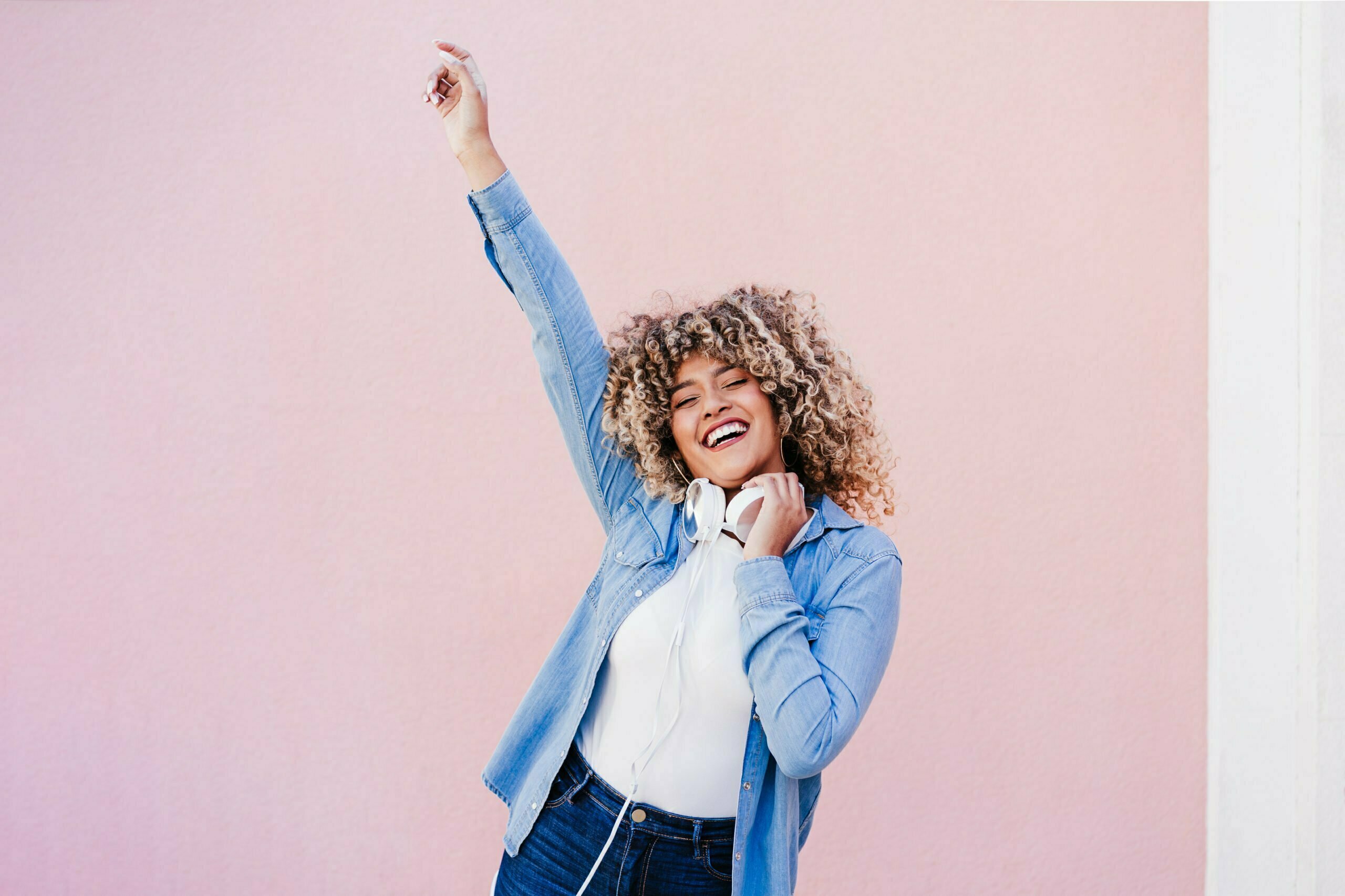 happy curvy hispanic woman with afro hair in city using mobile phone and headset